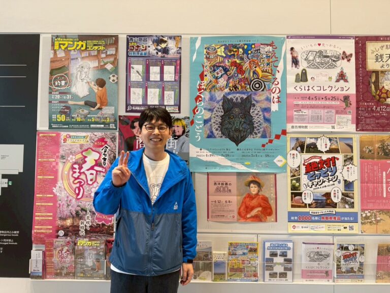 鳥取県立美術館に「もえているのはぼくらのこどう」の大きなポスターが貼られており、その前でピースして写るアーティスト・りょう