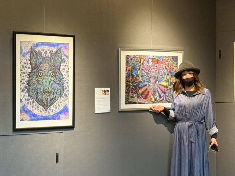 自分の作品と一緒に写るアーティスト・エンジェルユキ。こちらに手を振っているようなポーズ