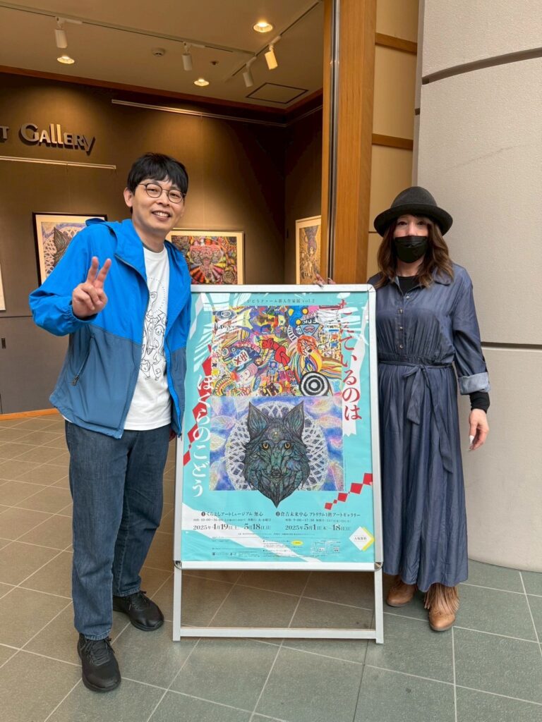 ポスターの前で記念撮影・ポスターを挟んで左にアーティスト・りょう、右にエンジェルユキ