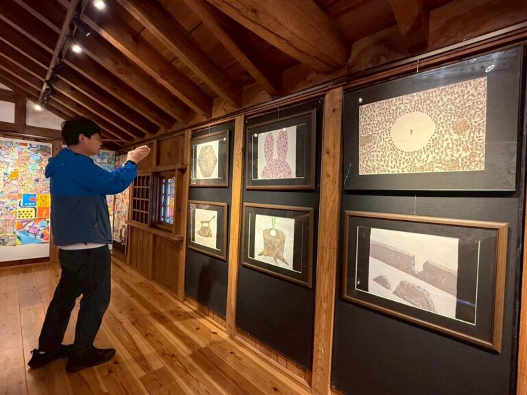 自分の作品ついて解説している?アーティスト・りょう。 おじさんを描いた作品が額装されて6作展示されている