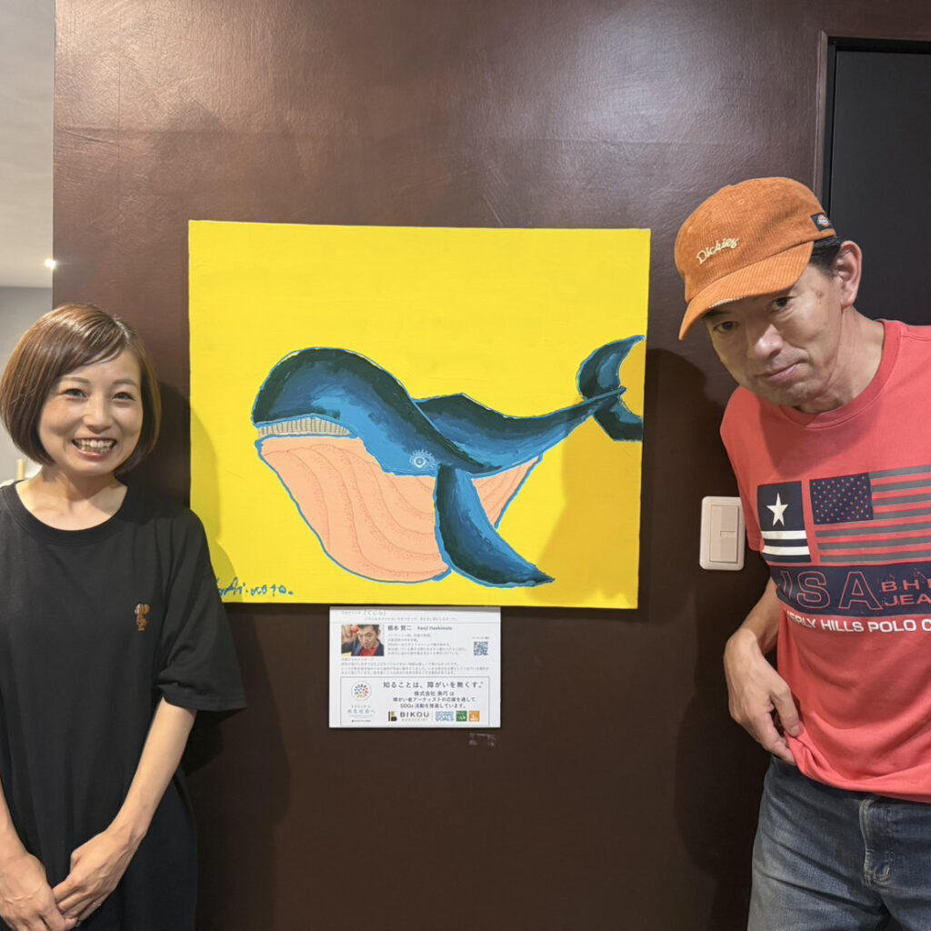納品した作品「くじら」のとなりに立っているアーティスト・橋本賢二と美巧の方