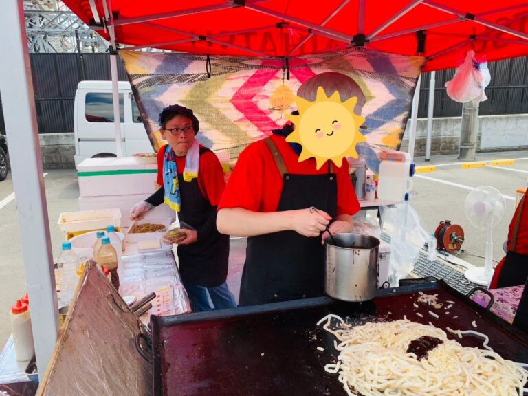 ダイハツマルシェでのようす ソースをかけようとしているメンバー