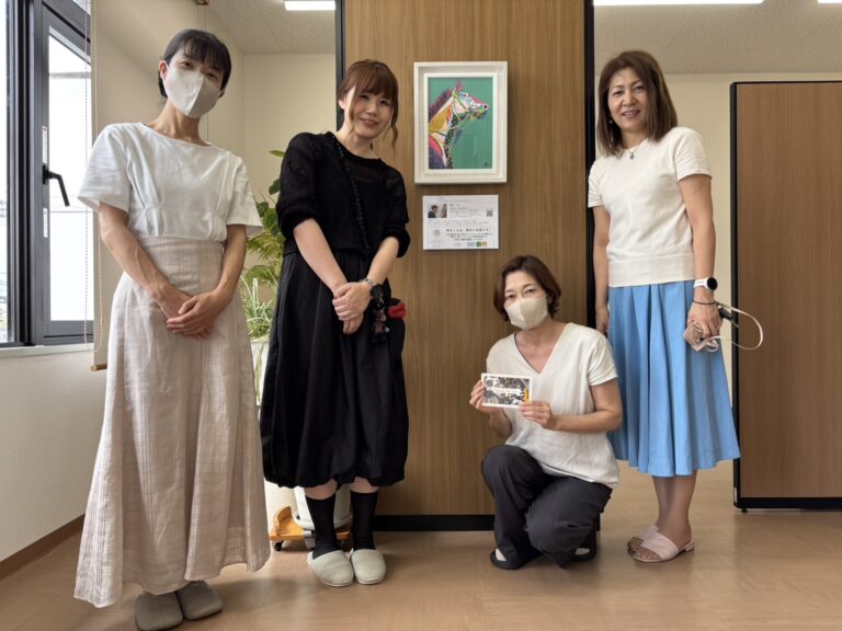 Rie作「POP」が柱に飾られている。その前で笑顔で写るRieと中川社労士事務所の3名