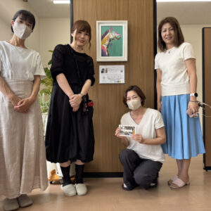 Rie作「POP」が柱に飾られている。その前で笑顔で写るRieと中川社労士事務所の3名