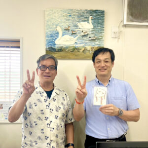 納品した作品の前でピースして写るアーティスト・川上岳史と日圧機販の方
