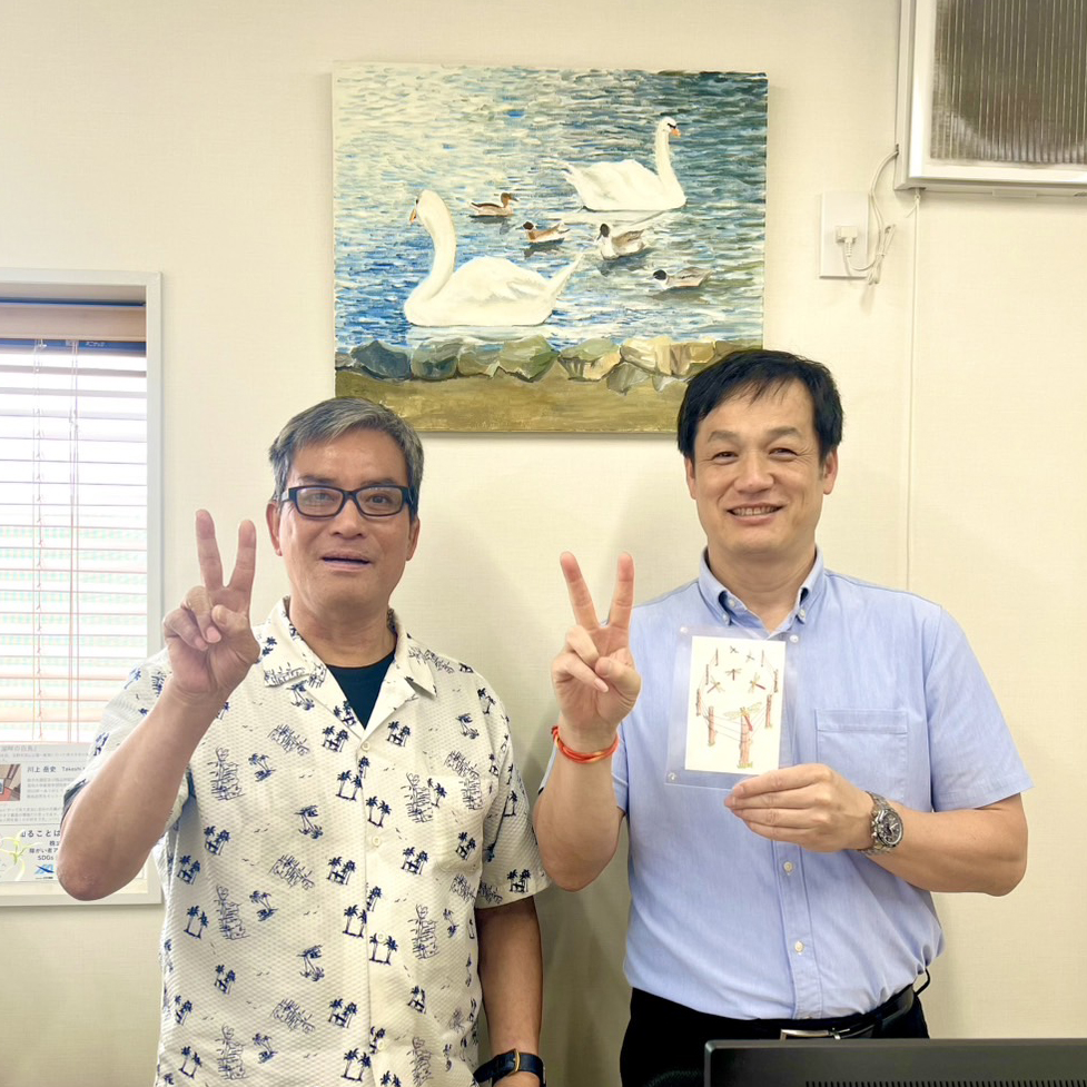 納品した作品の前でピースして写るアーティスト・川上岳史と日圧機販の方