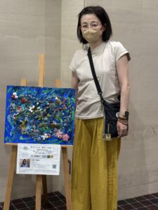 納品した自分の作品とその横に立つアーティスト・小林智恵子