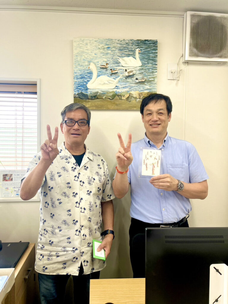 納品した作品の前でピースして写るアーティスト・川上岳史と日圧機販の方