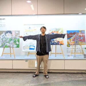 展示ケースの前で腕をひろげて写るアーティスト・Miya