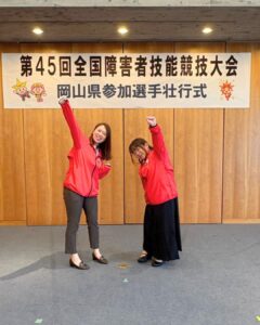横断幕の下でえいえいおー!のポーズをとるろりちゃんと荒谷マネージャー