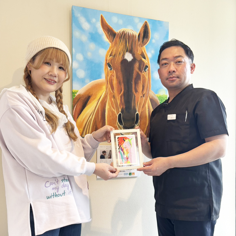 サンクスカードを渡すアーティスト・Rie（左）ときらり歯科の先生（右）うしろには納品した作品