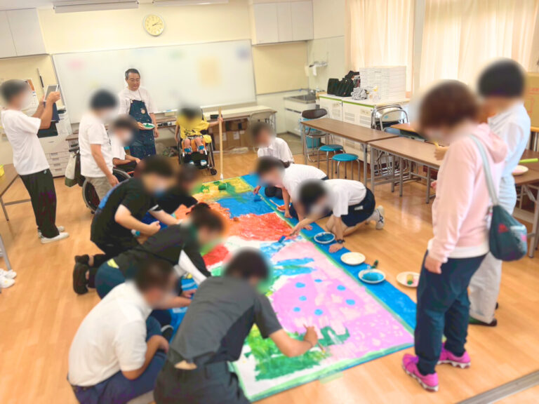 １ｍ×２ｍの大きな紙に自由に絵を描く東支援学校の生徒たちとそれを見守るアーティスト・下村良作