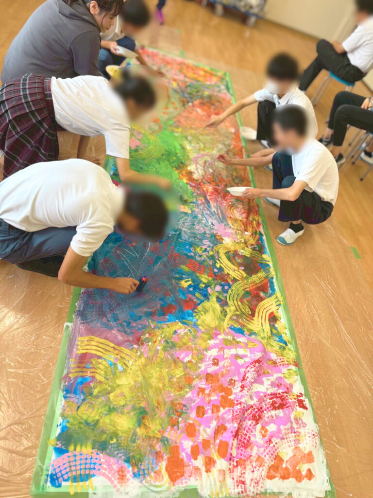 １ｍ×２ｍの大きな紙に自由に絵を描く東支援学校の生徒たちとアーティストしゃけ。