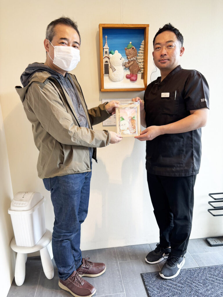 きらり歯科院長（右）にサンクスカードを手渡すアーティスト・下村良作（左）