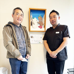 納品したアーティスト・下村良作 作「ともだちマフラー」（中央）と下村良作（左）きらり歯科院長（右）
