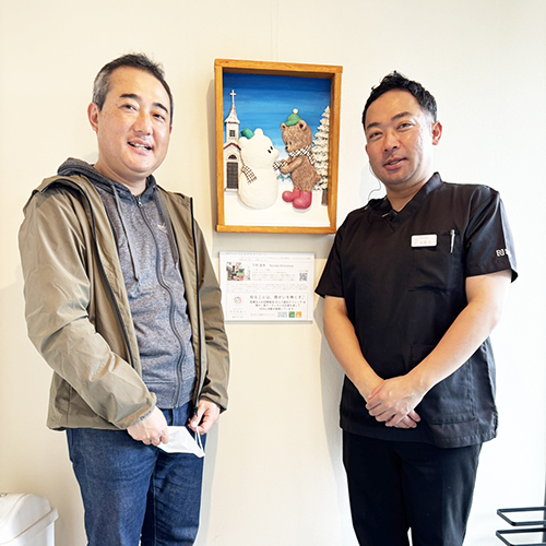 納品したアーティスト・下村良作 作「ともだちマフラー」（中央）と下村良作（左）きらり歯科院長（右）