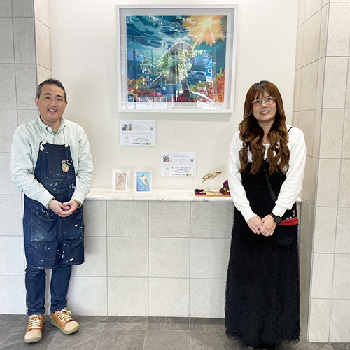 納品した作品の前で笑顔で写るアーティスト・下村良作とアーティスト・Rie