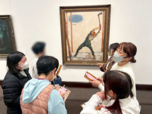 木こりの絵を鑑賞しながら俳句を考えているアーティスト・カスミン、ろりちゃん、てれさ、メンバー・まみ、わかなちゃん、菱野マネージャー