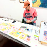 アーティスト・橋本賢二のブース 机の上には花を描いたサンクスカードがずらりと並んでいる