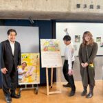 入口のポスター前に立っているパートナー企業の方(左)とアーティスト・Miya(中央・腕を縦に広げてポーズをとっている)とアーティスト・Rie