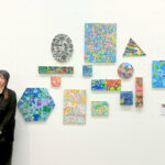 アーティスト・かなっぺを彼女の作品コーナーの前で撮影した写真 左端にかなっぺ、視線は右下にそれており若干変顔