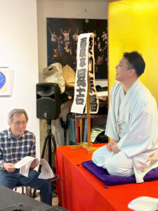 落語を披露する昇吉様と脇で台本を確認するアーティスト・土肥ヨシ