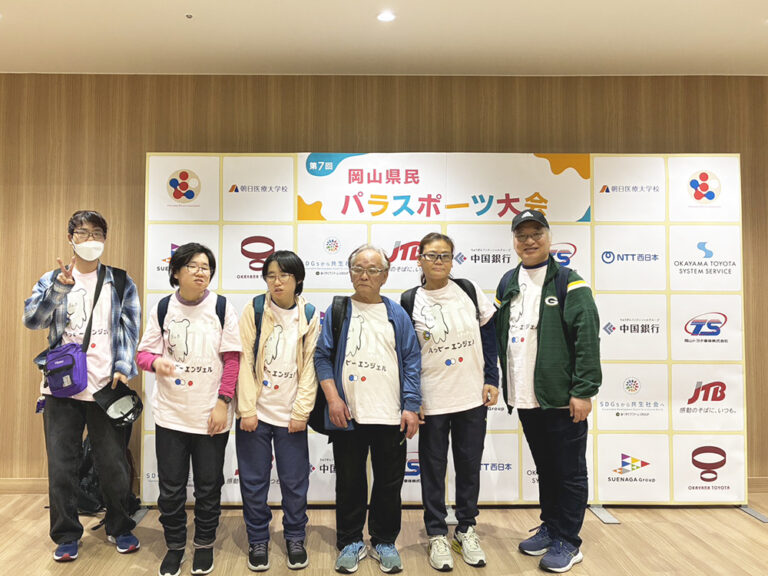 大会記念ボードの前に立って写るハッピーエンジェル